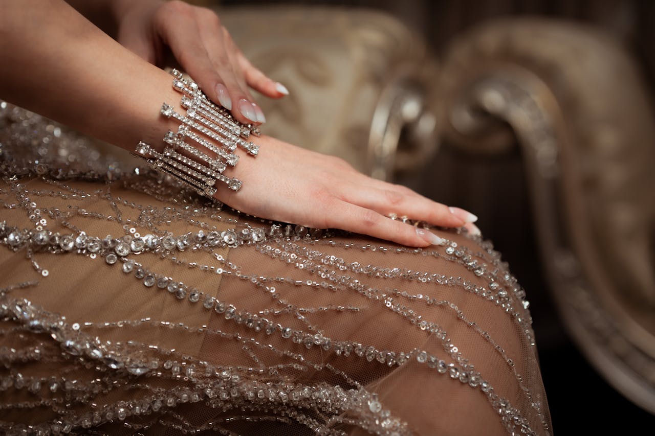 Close-up of a womans hand with a diamond bracelet on a beaded dress in an elegant setting.