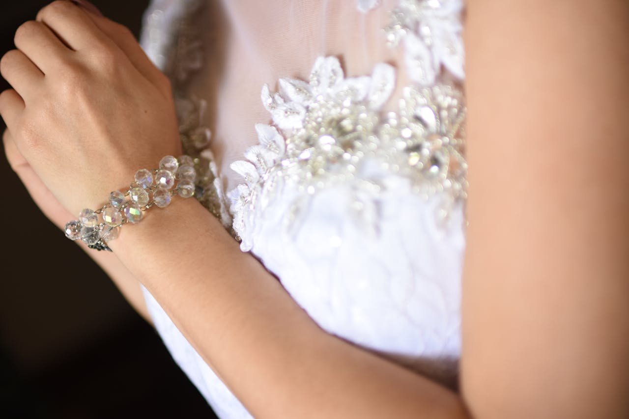 Close-up of a womans bracelet complementing a lace-embellished bridal gown, showcasing elegance.
